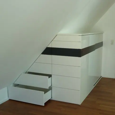 Weiße Schubladenelemente mit dunklem Band unter einer Dachschräge