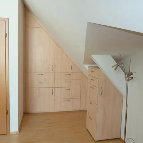 Schrankwand aus hellem Holz mit Schubladen unter einer Dachschräge