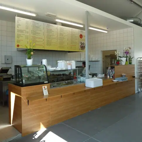 Theke mit Holzfront in einem Imbiss, dahinter Speisekarten an der Wand